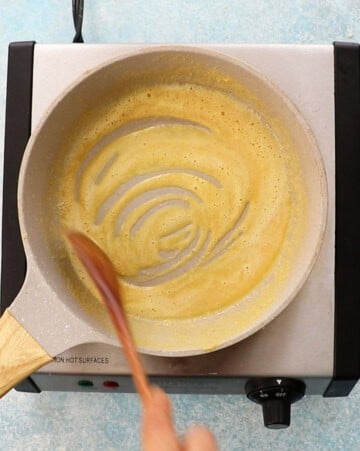 a hand toasting chickpea flour in a white skillet.