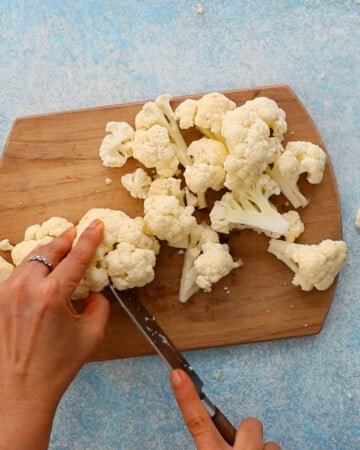 two hands cutting a cauliflower into florets.