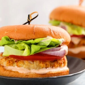 one assembled chicken burger placed on a black round plate.
