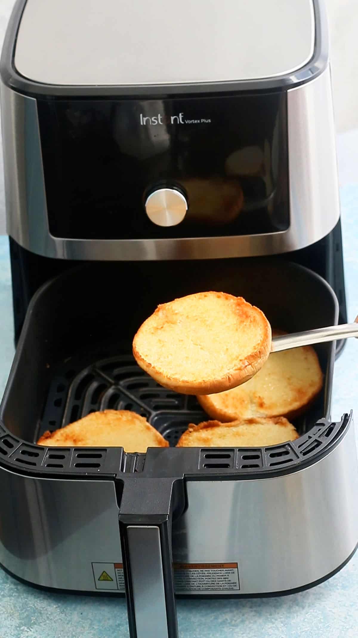 a hand lifting one toasted burger bun from an air fryer basket.