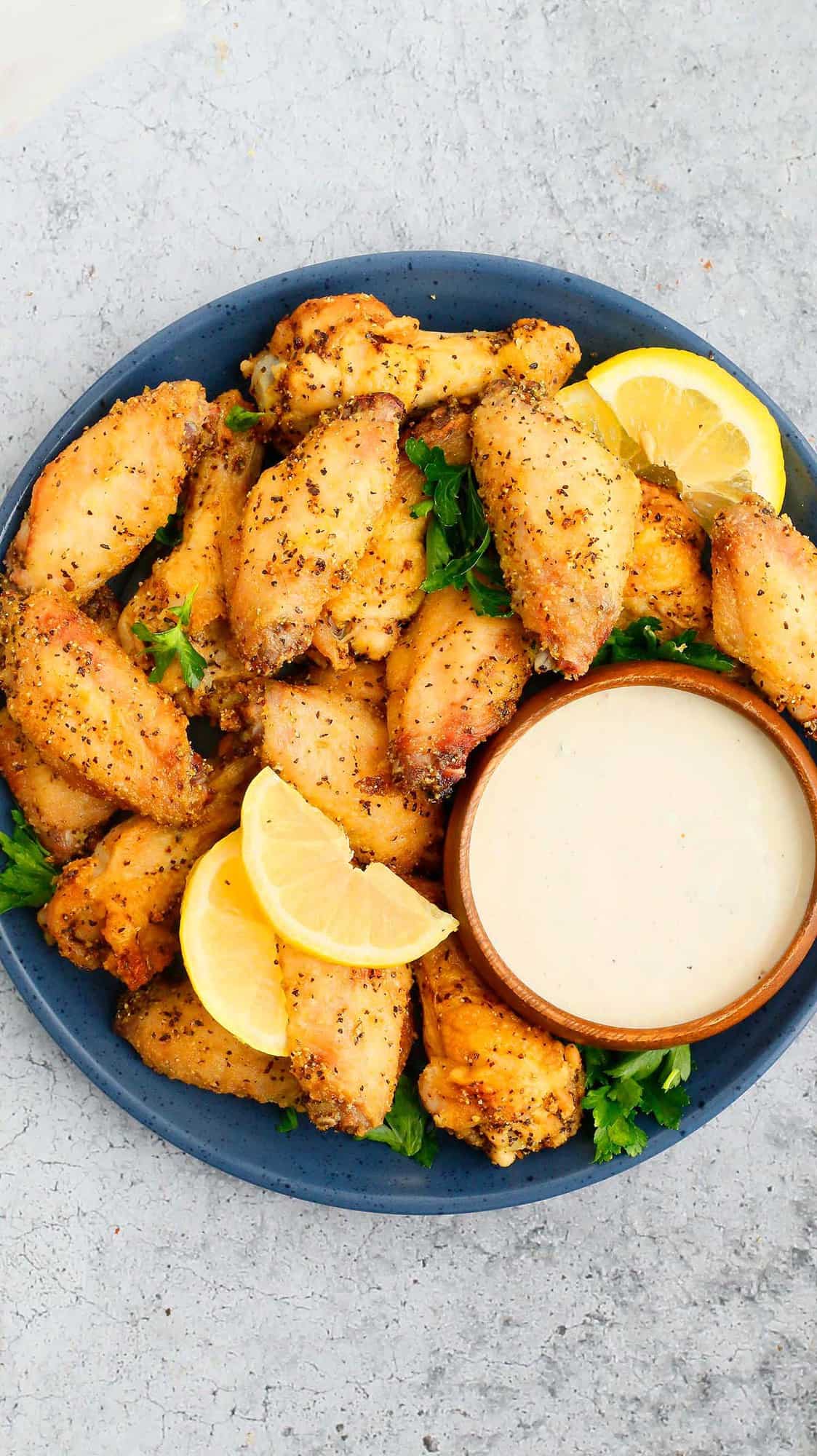 a blue round plate with air fryer lemon pepper wings with a bowl of ranch. 