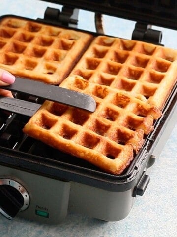 a hand removing one cooked waffle from a waffle maker.