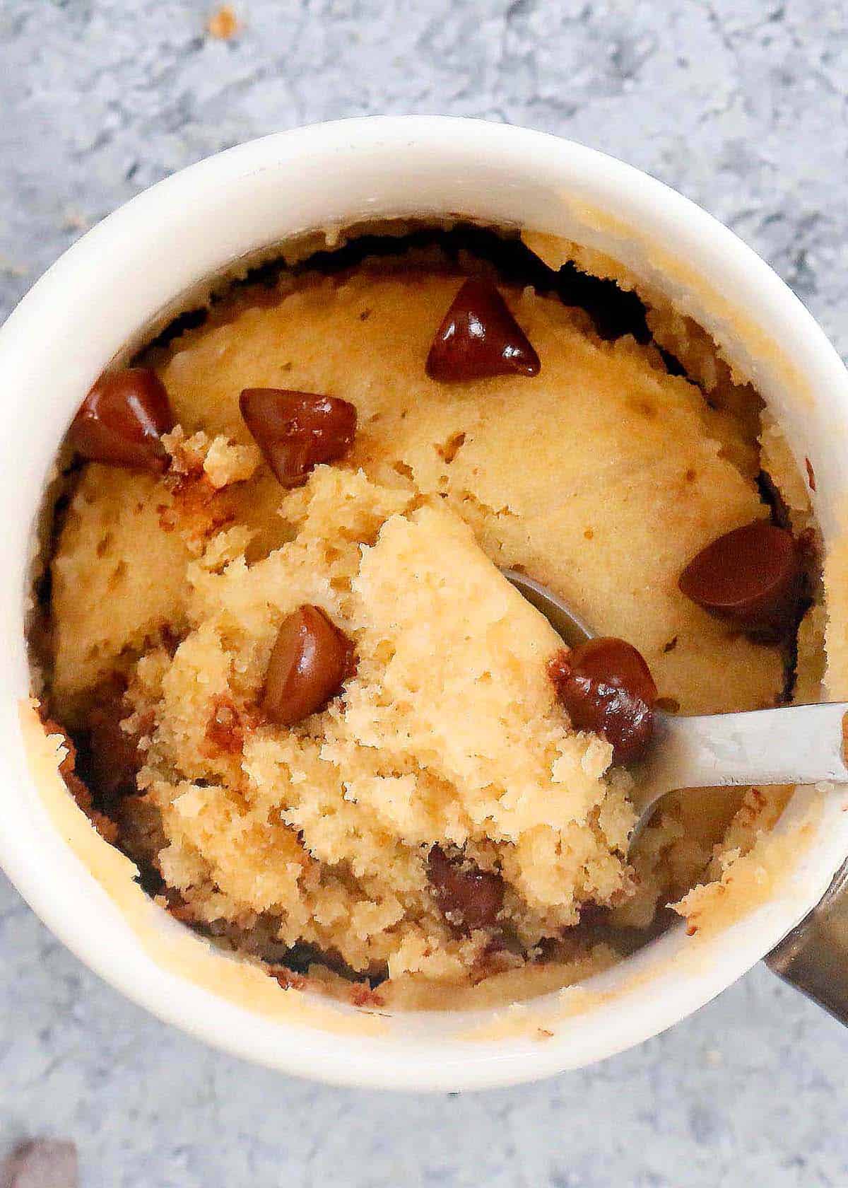 vanilla chocolate chip vegan mug cake in a white coffee mug along with a spoon.