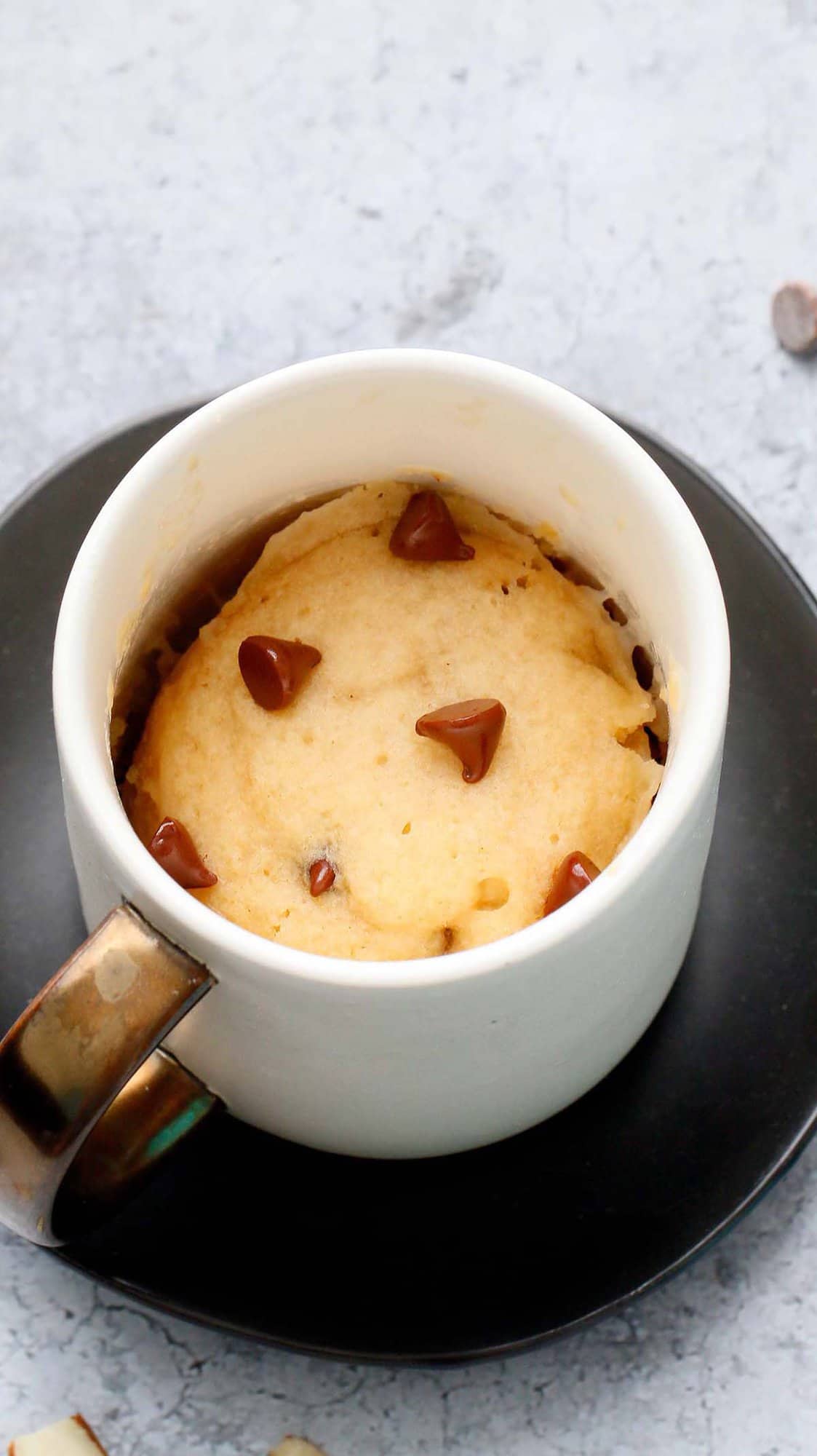 white coffee mug with vanilla cake topped with chocolate chips.