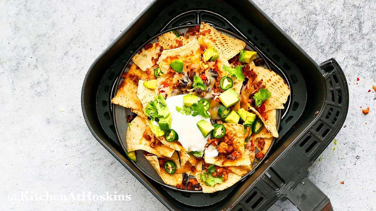 air fryer basket with black bean nachos topped with sour cream.