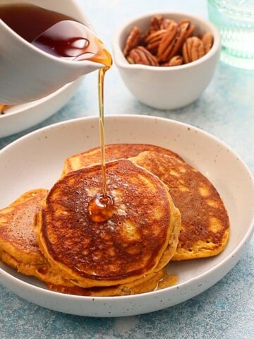a hand pouring syrup on 3 pancakes on a white plate.