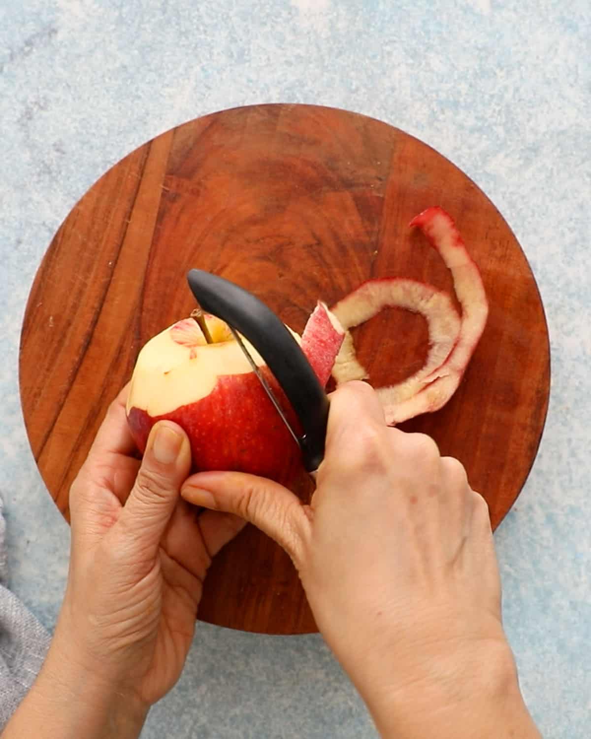 two hands peeling the skin of an apple.