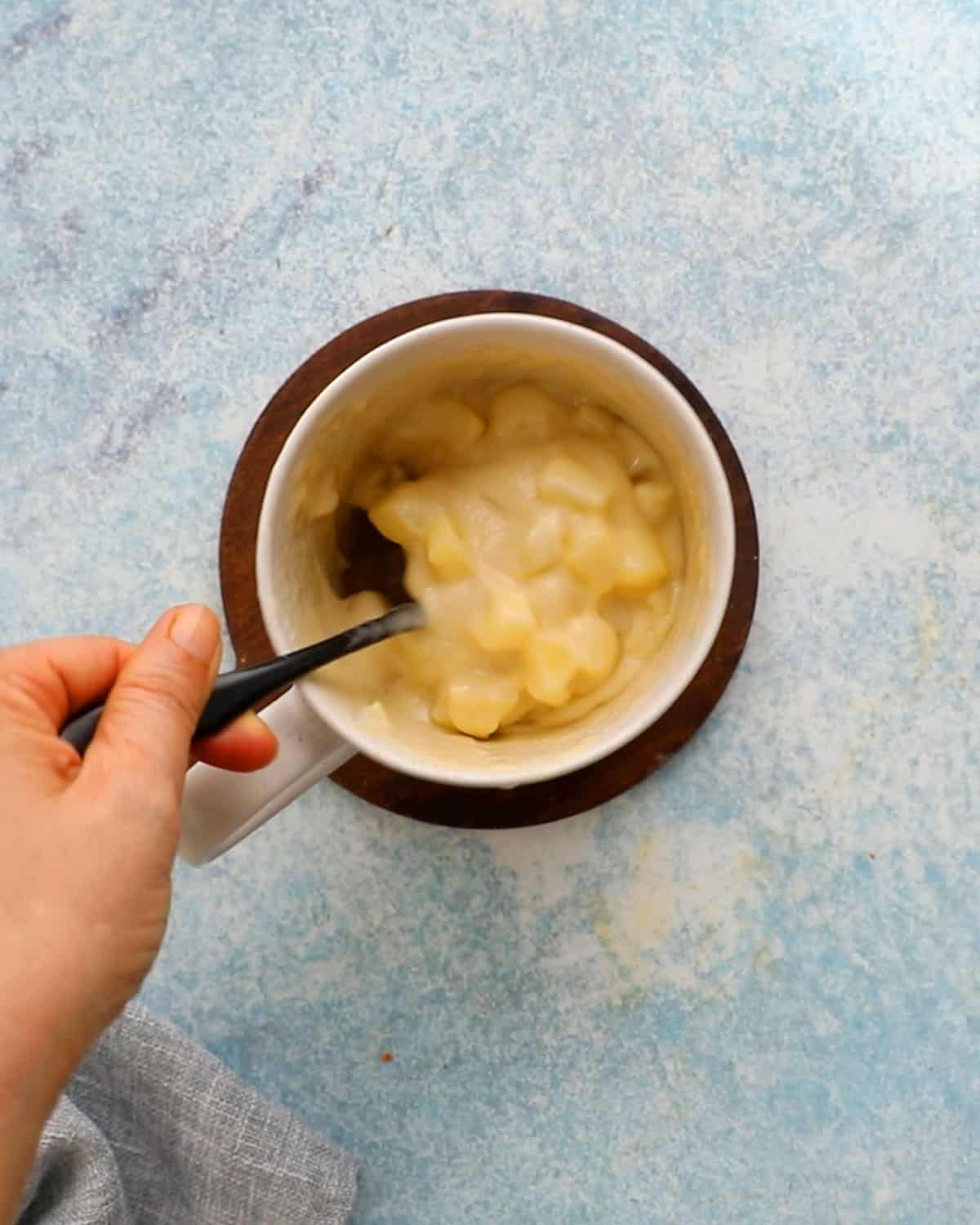 a hand mixing apple cake batter in a white mug.