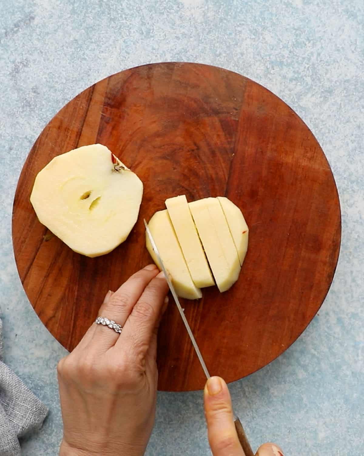 two hands cutting an apple intoo sticks.