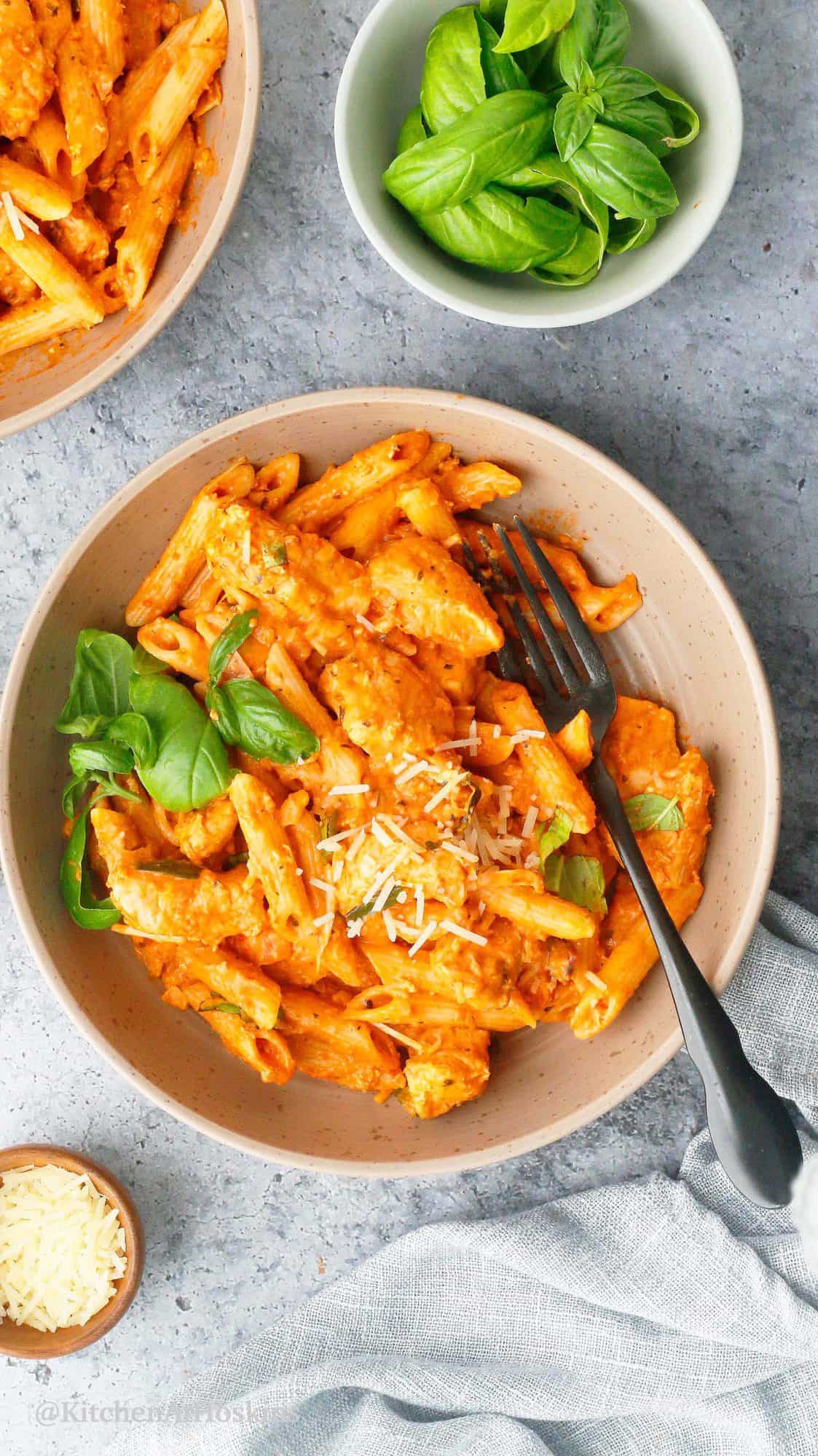 vodka sauce pasta with chicken served in bowls and topped with fresh basil.