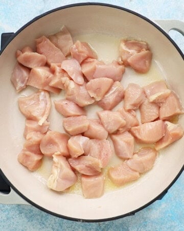 chicken pieces cooking in a white pan.