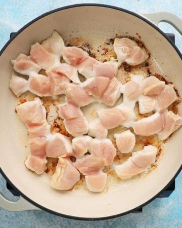 chicken pieces cooking in a white pan.