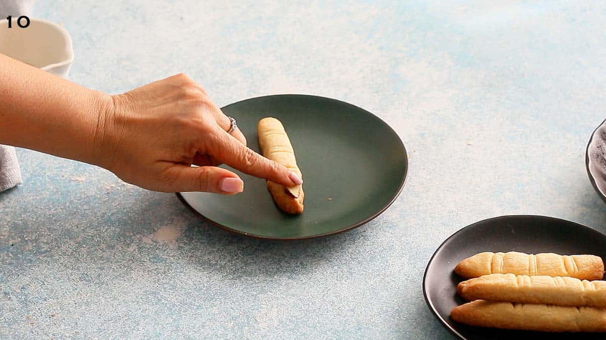 a hand fixing a sliced almond on top of finger cookie.