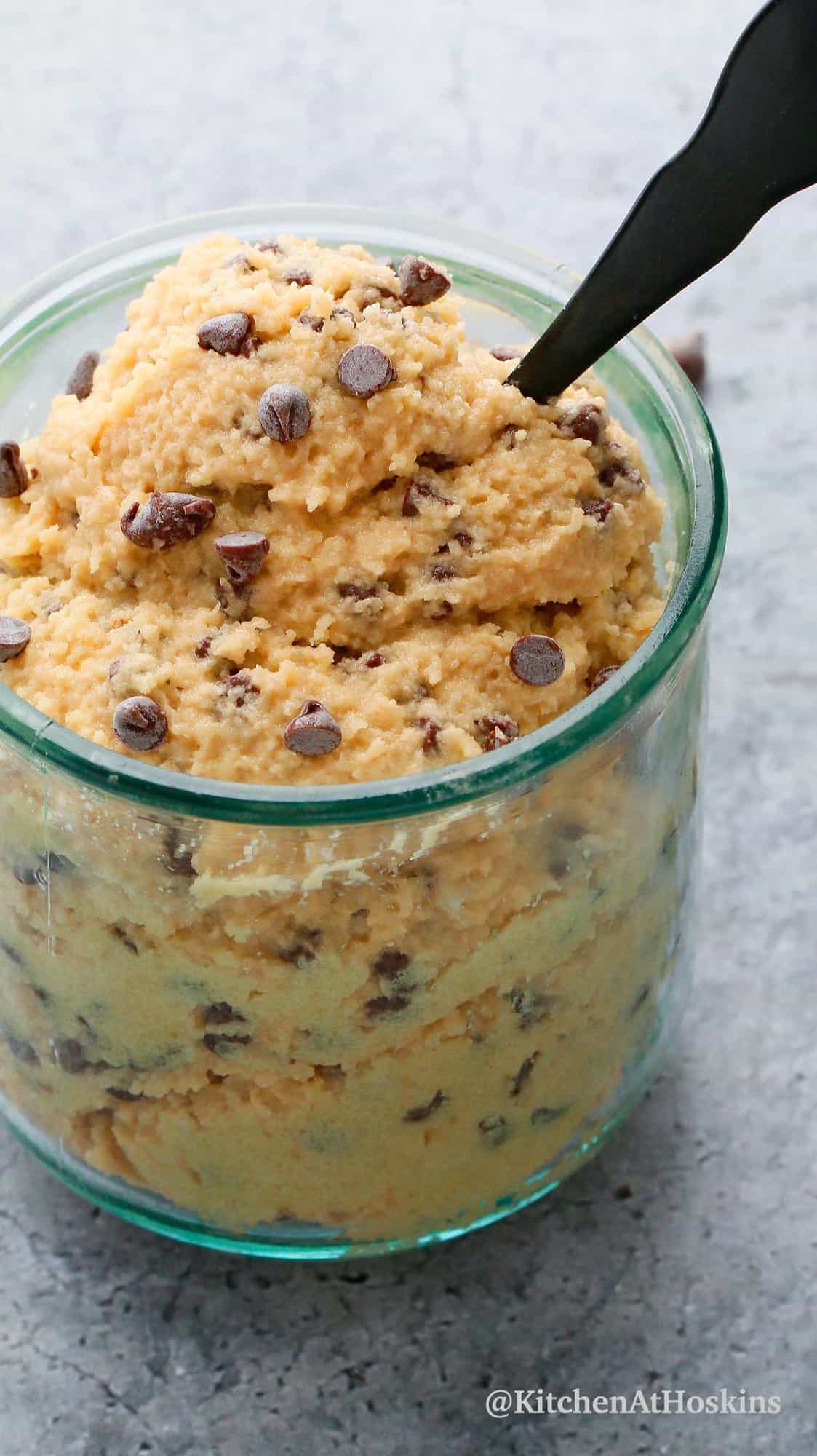 chocolate chip gluten free cookie dough in a glass with a black spoon.