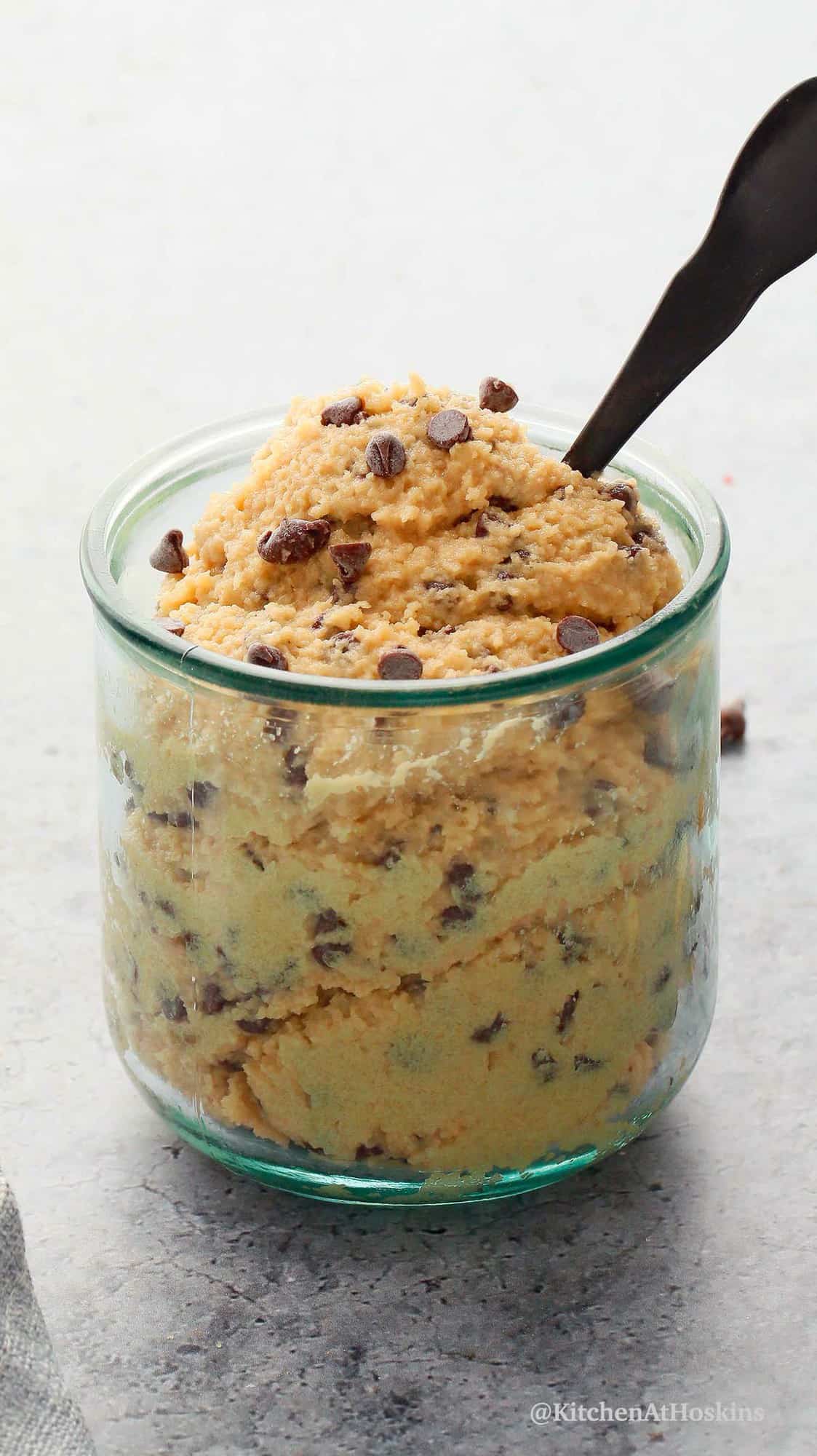 a glass jar filled with raw cookie dough along with a black spoon.