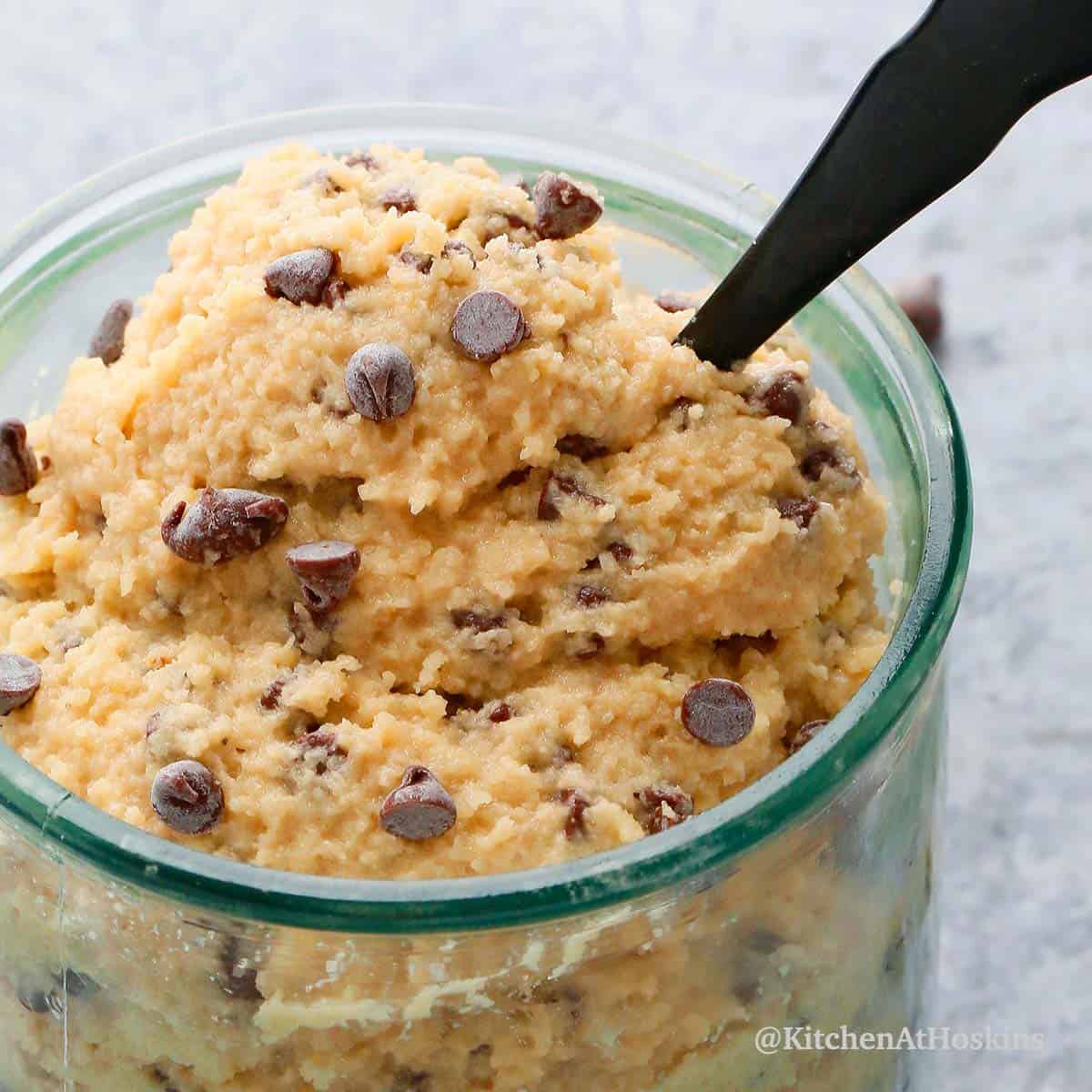 chocolate chip gluten free cookie dough in a glass with a black spoon.
