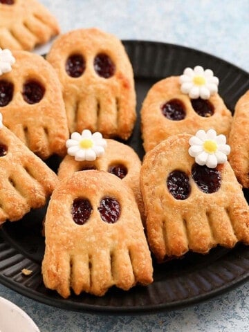 Halloween pop tarts in the shape on ghosts placed on a black plate.