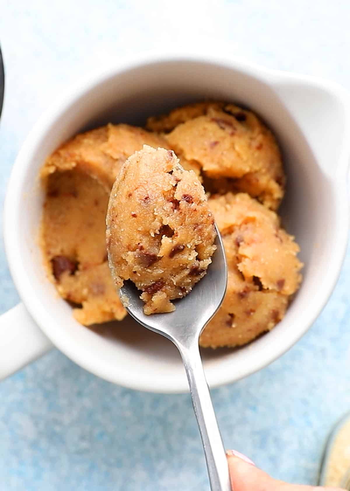 a spoonful of raw cookie dough above a white bowl filled with the same.