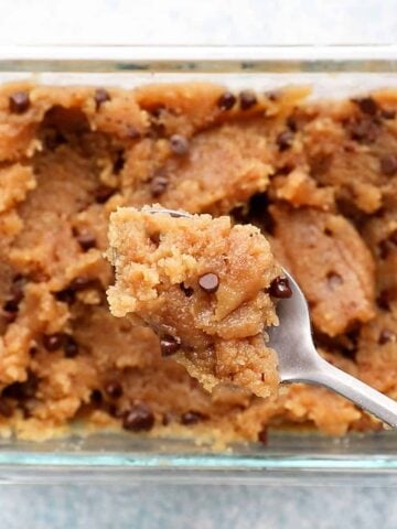 a spoonful of chocolate chip cookie dough above a glass dish filled with the same.