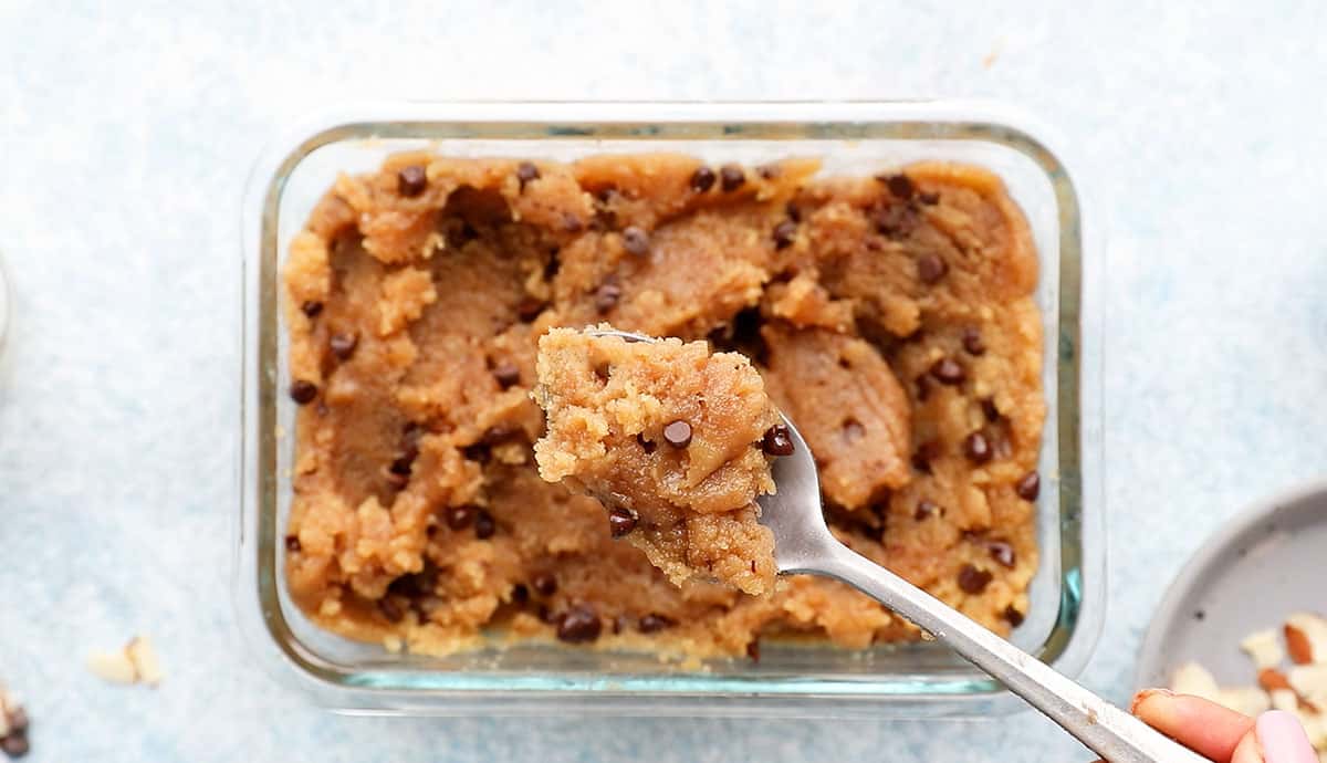 a spoonful of raw cookie dough above a rectangular glass dish filled with the same.