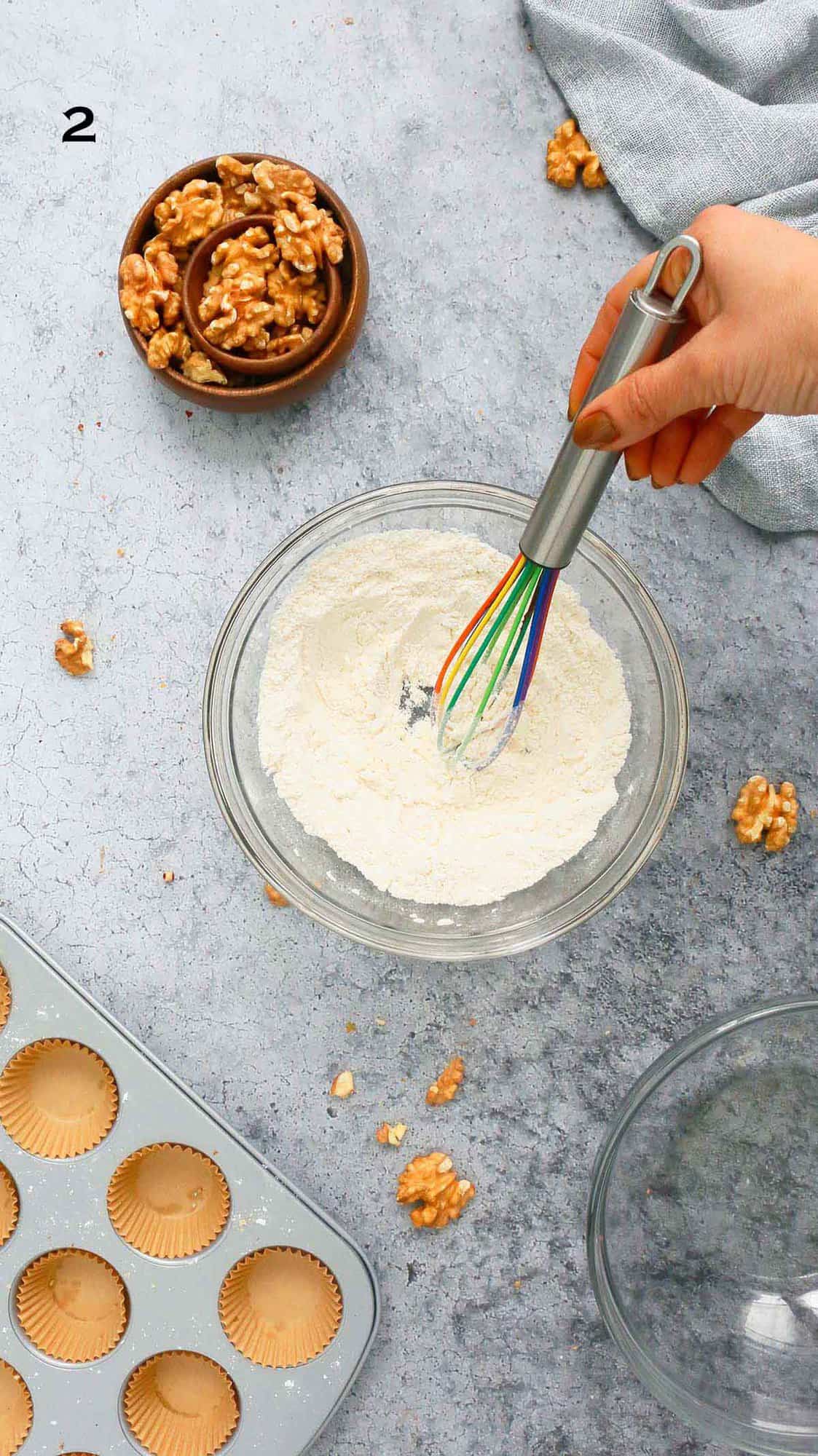 a hand whisking flour in a glass bowl. 