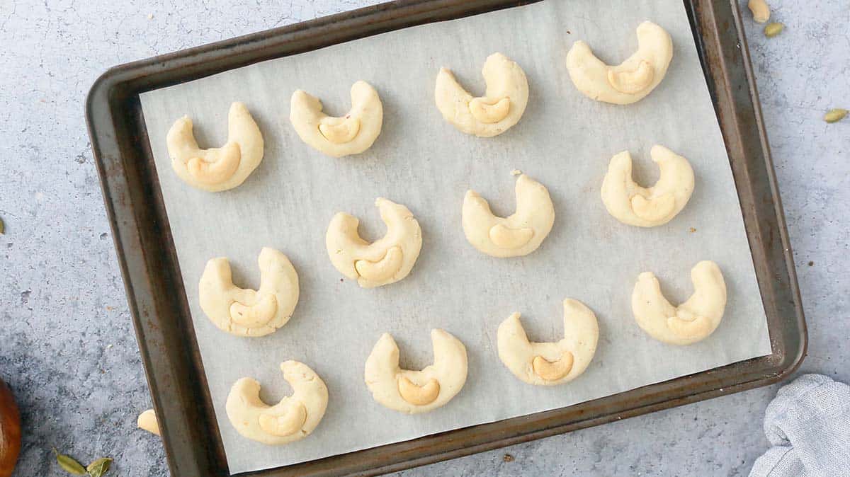 Crescent shaped cardamom cookie dough on a baking sheet. 