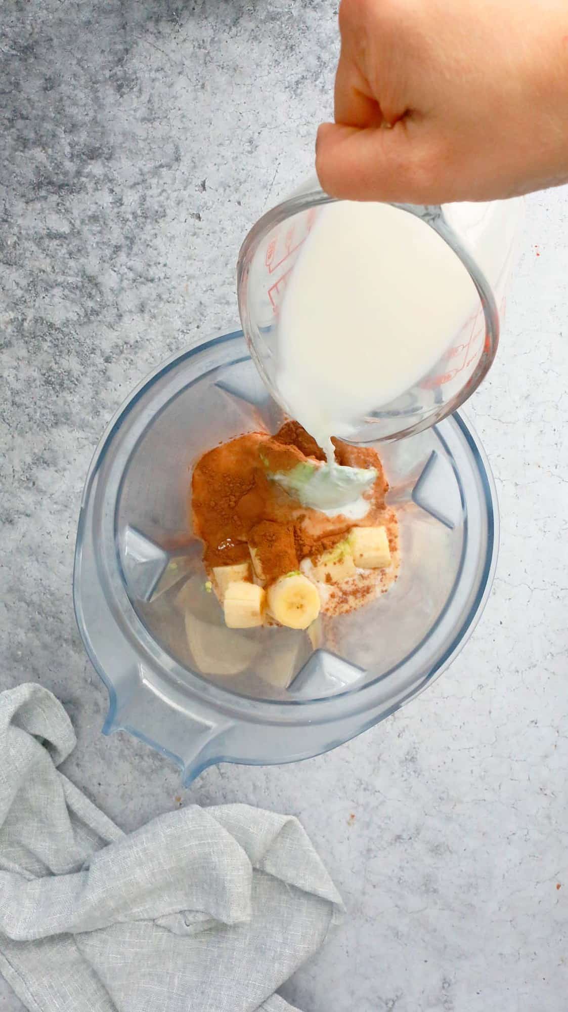 pouring milk into a blender with banana, cocoa powder and avoacdo.
