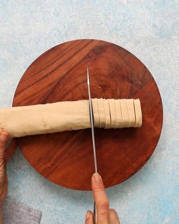 a hand slicing pinwheel cookie dough log into slices.