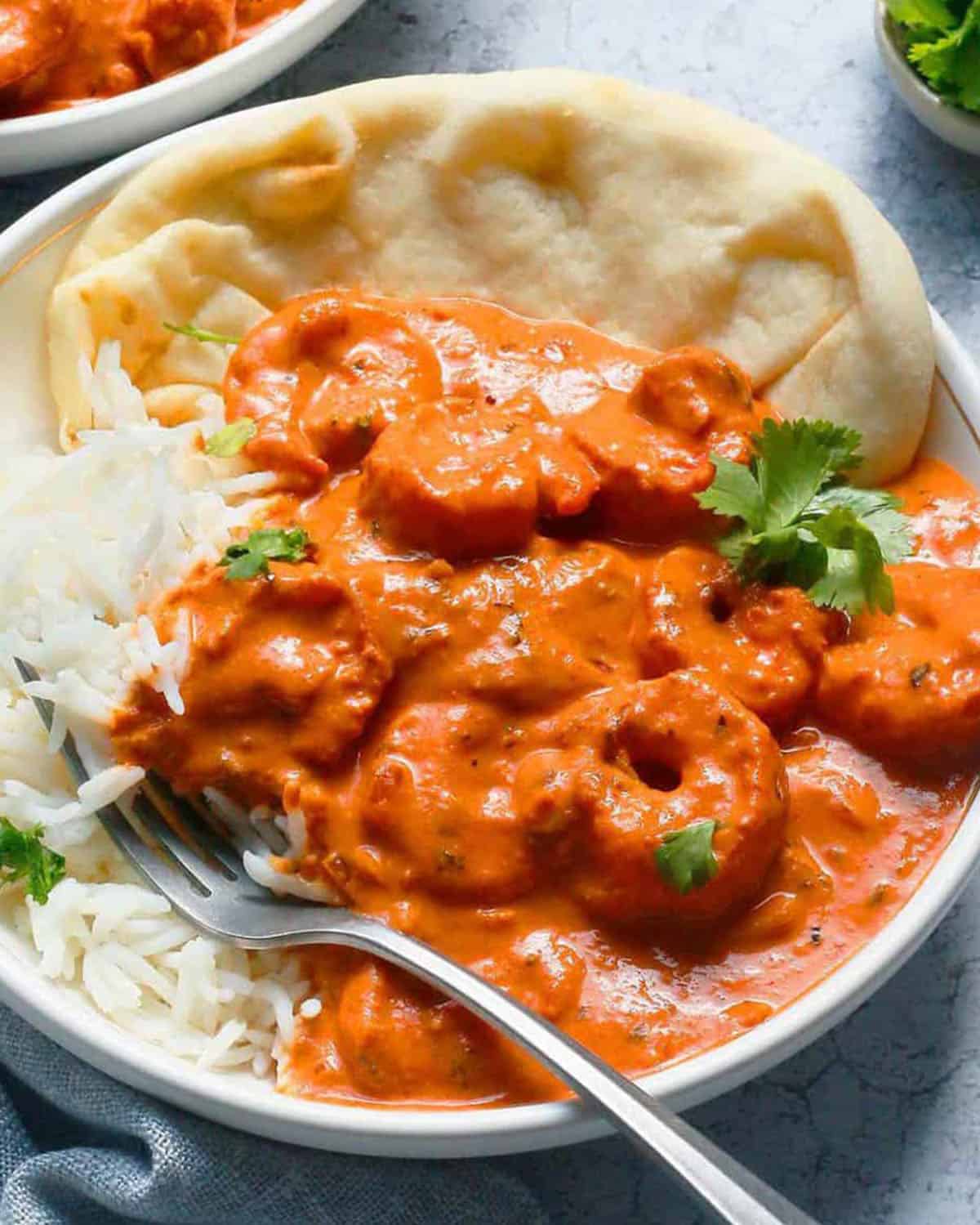 orange buttered shrimp curry in a white bowl along with white rice and spoon.