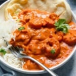 orange buttered shrimp curry in a white bowl along with white rice and spoon.