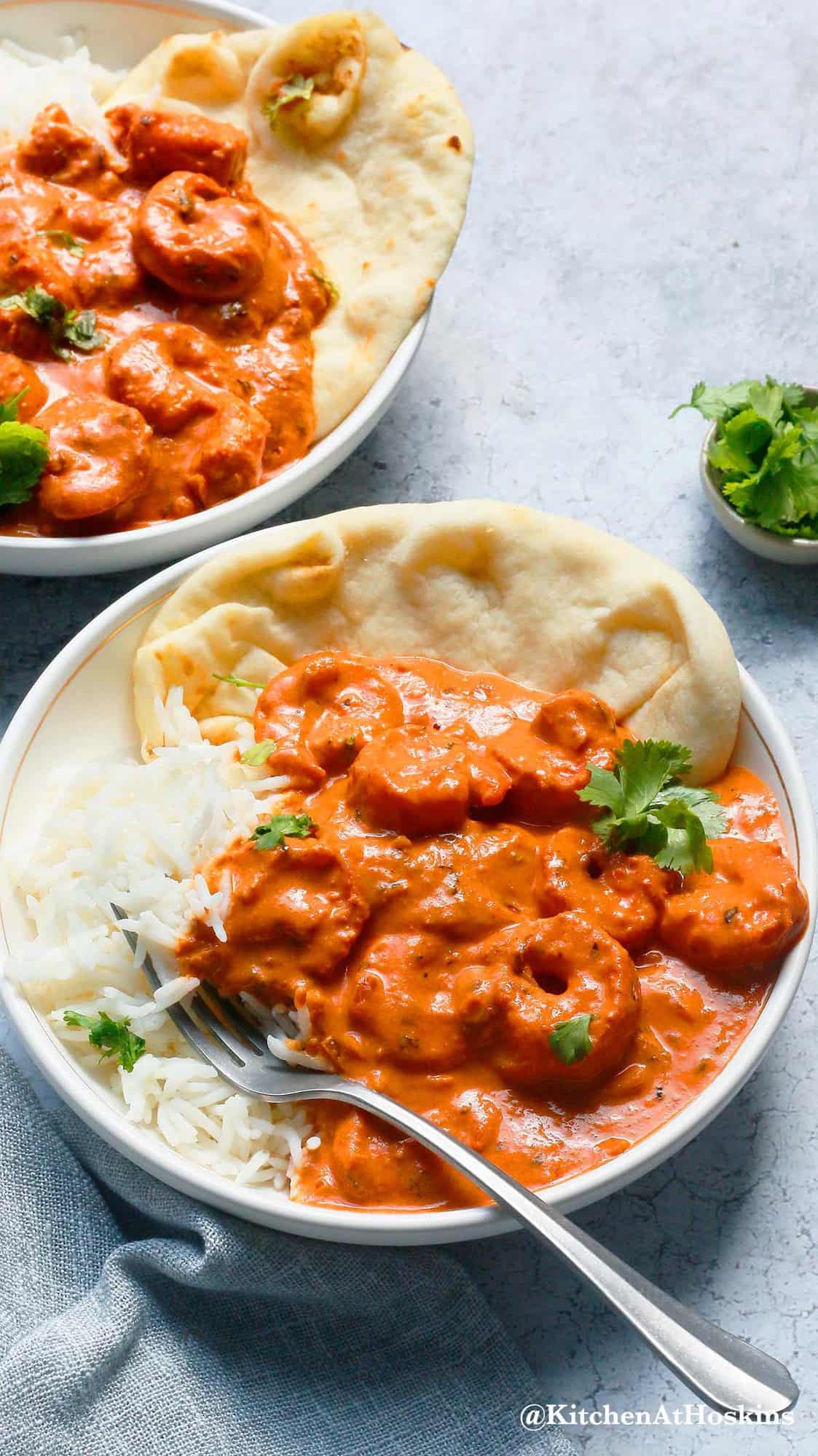 white bowls with shrimp in Indian butter sauce with naans.