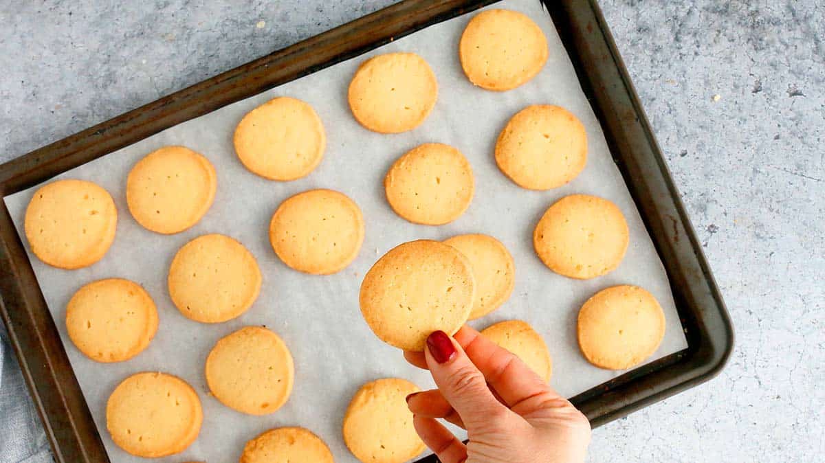 hand holding a shortbread cookie made with brown sugar above a baking sheet.