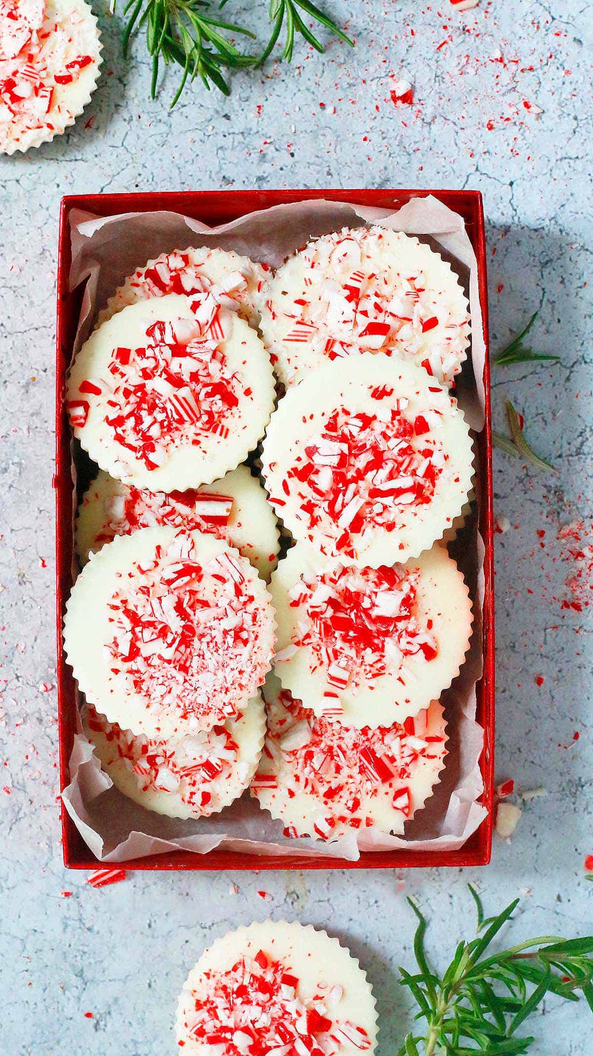 a red gift box filled with chocolate peppermint bark rounds.