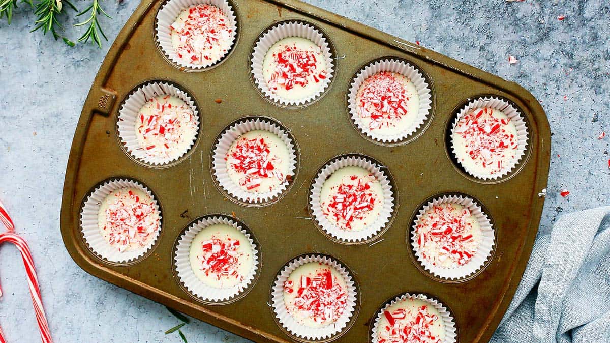 a muffin pan with set chocolate bark topped with crushed candy canes.