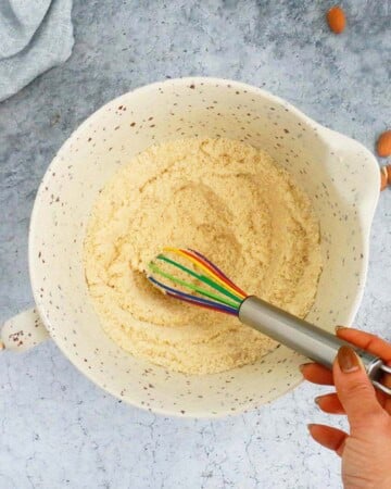 a hand mixing flour in a white bowl using a whisk.