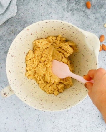 a hand mixing almond flour cookie dough in a white bowl.