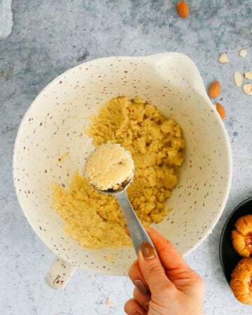 a hand holding one tablespoon of cookie dough above a bowl.