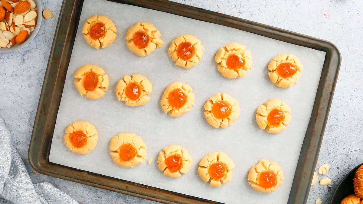 shaped orange thumbrpint cookie dough in a white paper lined baking sheet.