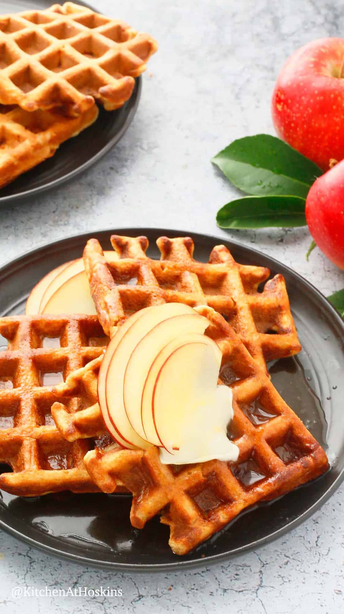 3 waffles on a black plate topped with sliced apples.