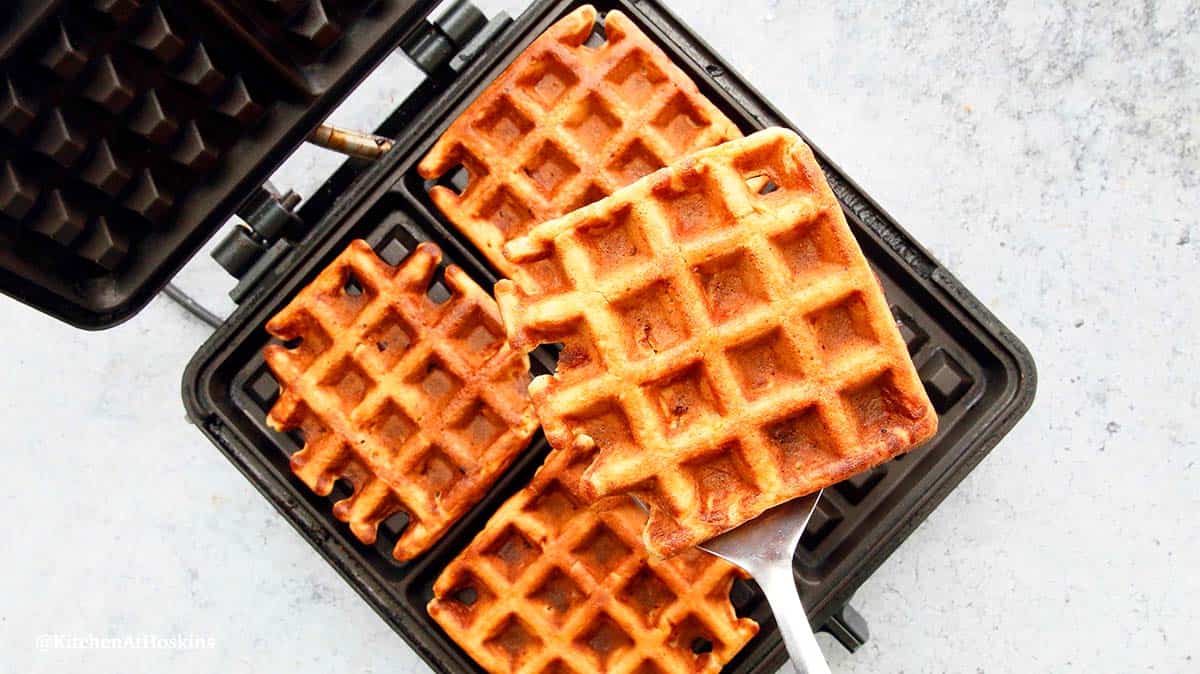 a apple waffle on a spatula on top of hot waffles in iron.