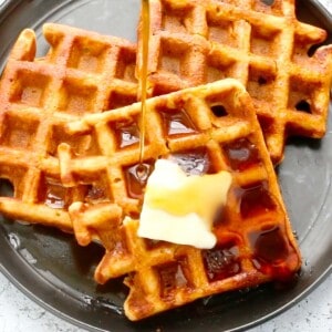 black plate with 3 waffles with a slab of butter and syrup.