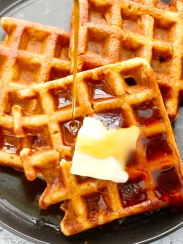 black plate with 3 waffles with a slab of butter and syrup.