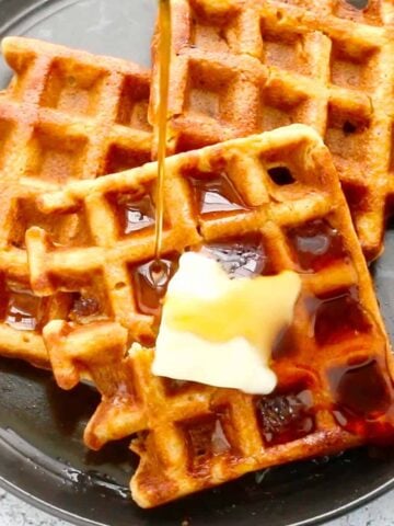 black plate with 3 waffles with a slab of butter and syrup.