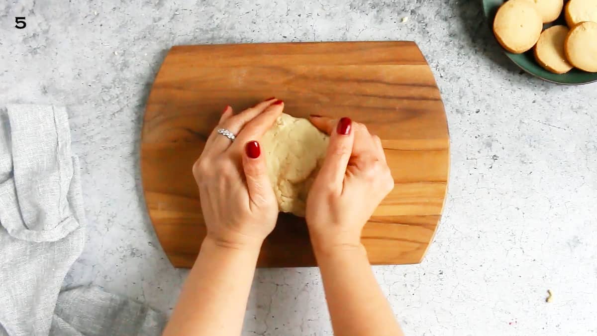 2 hands shaping cookie dough on a wooden board.