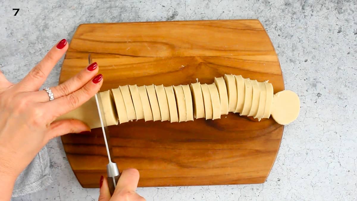 a hand slicing a cookie dough log into slices using a knife.