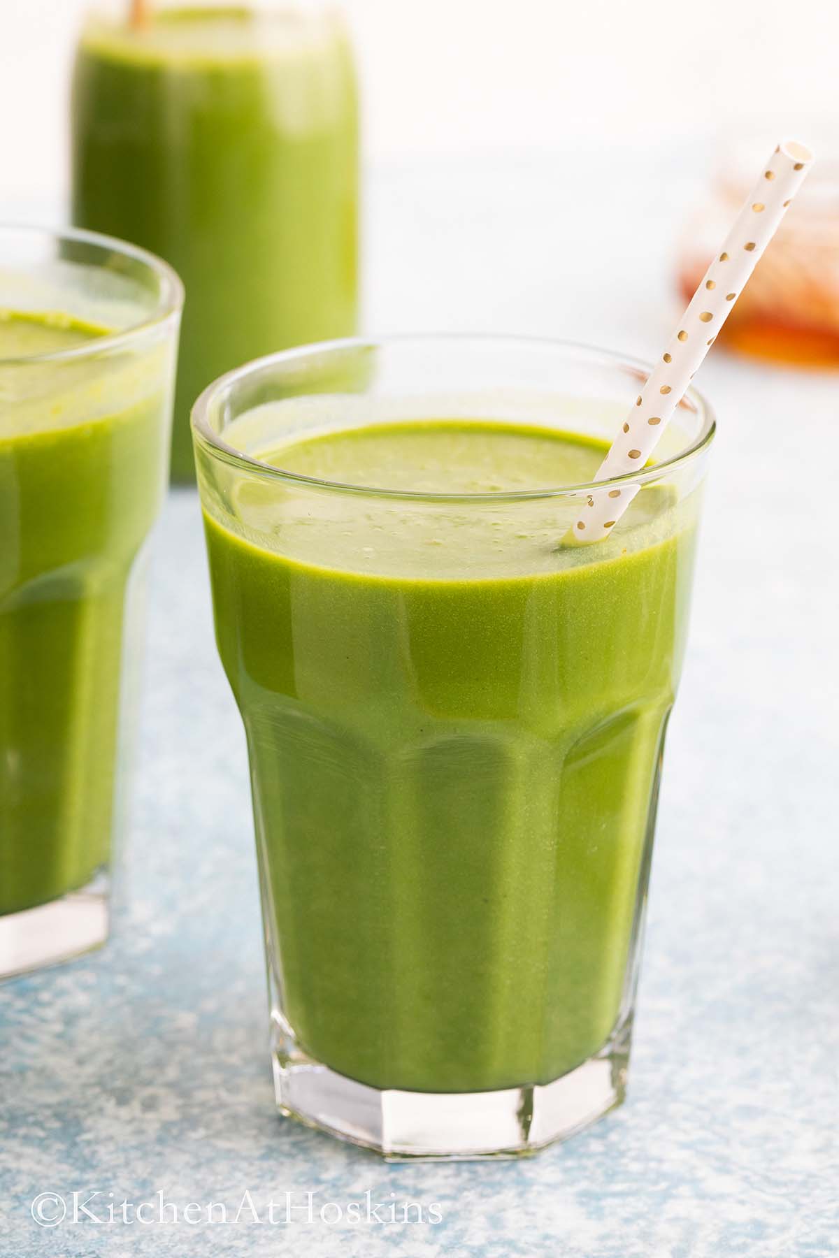 glasses filled with green smoothie along with straws.