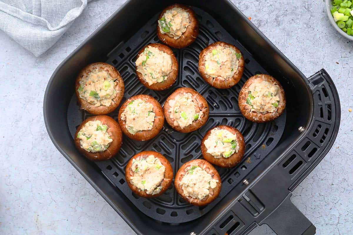 air fryer basket with filled mushroom caps, ready to be air fried.