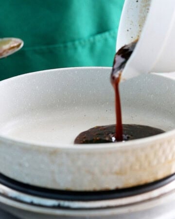a hand cooking brown teriyaki sauce in a grey skillet.