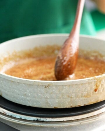 a hand cooking brown teriyaki sauce in a grey skillet.
