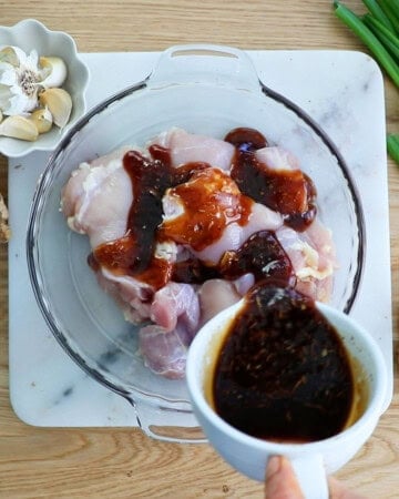 a hand mixing brown teriyaki sauce over pink chicken.